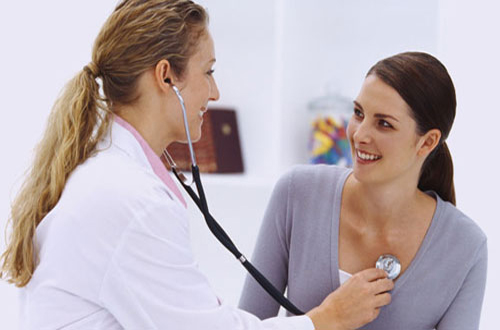 Side profile of a female doctor examining a young woman's chest with a stethoscope